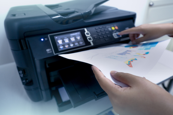 Close-up of hands using an office laser printer, with a printed document showing colorful charts and graphs being retrieved from the machine.