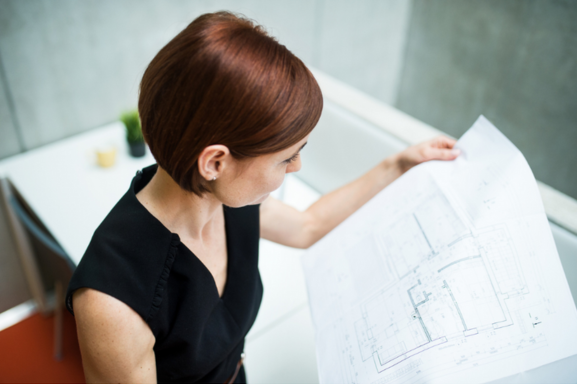 A woman examining detailed architectural plans in an office, showcasing the high-quality output of a large format printer for complex documents and designs.