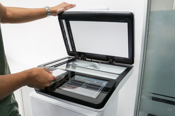 A person using an office multifunction printer with a touchscreen interface, scanning a document in a modern workplace setting.